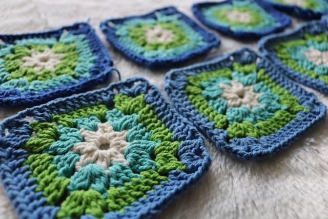 Plusieurs travaux de crochet colorés en cours disposés sur une table avec du fil et des crochets